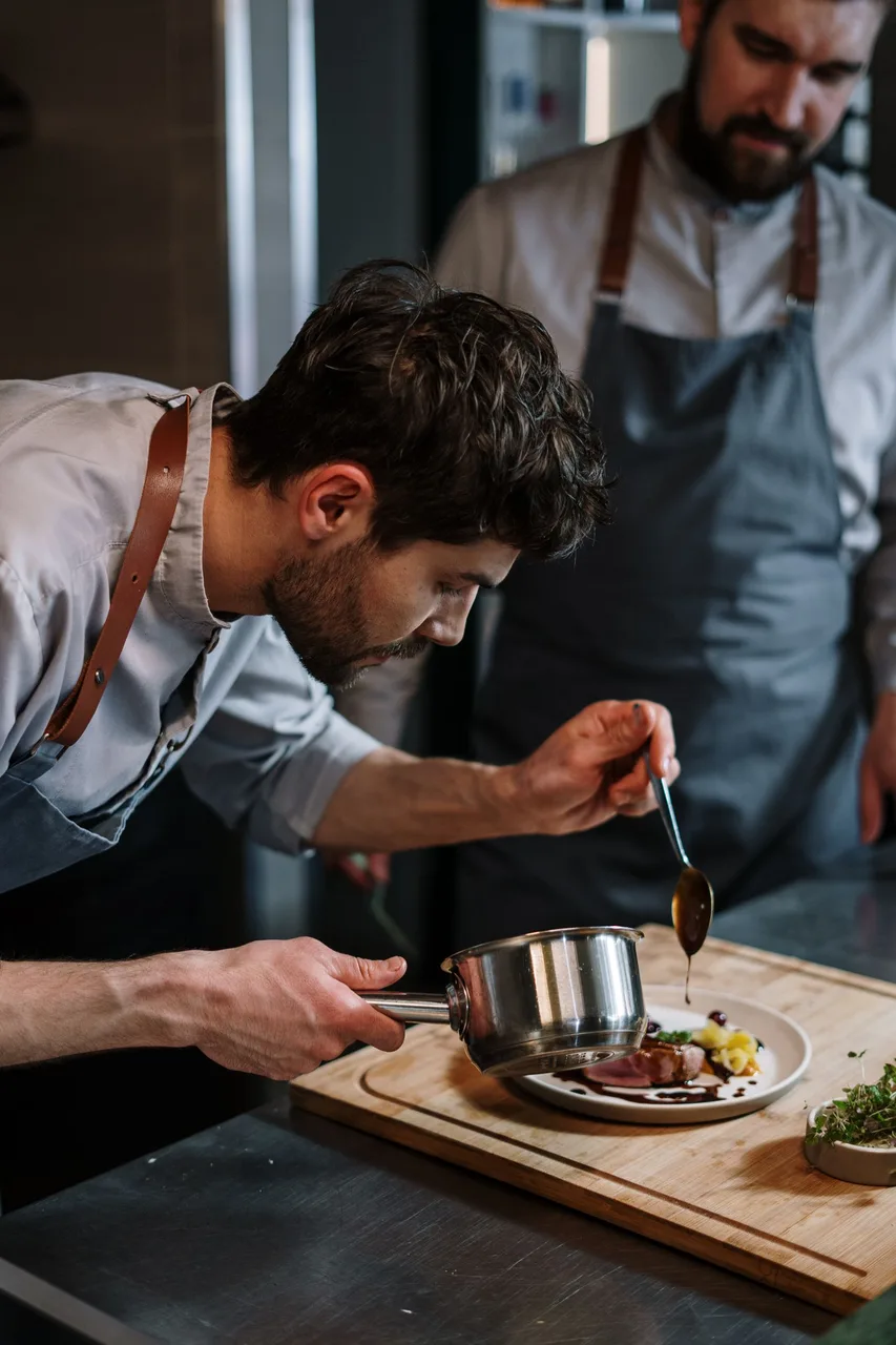Um cozinheiro rega o prato com o molho da panela