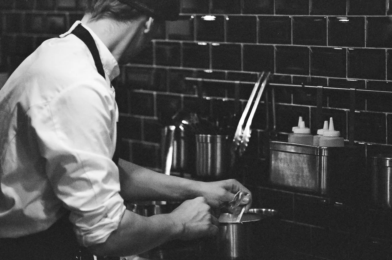 Um cozinheiro de branco trabalha na bancada de uma cozinha profissional